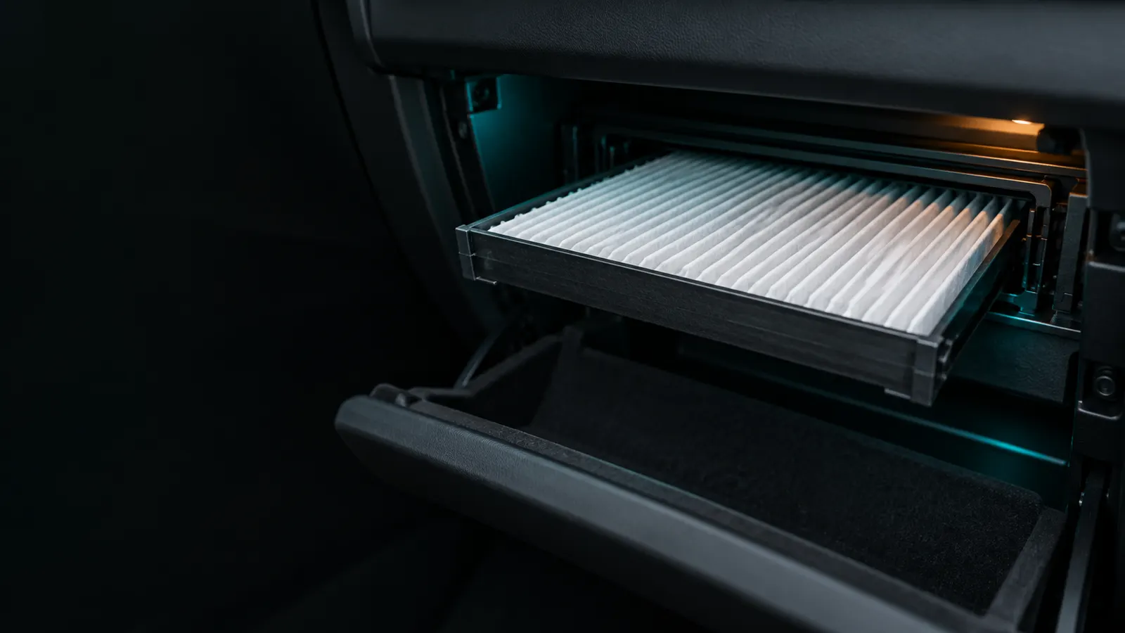 Illustration of a pleated cabin air filter being slid out of its housing behind an open glove box.